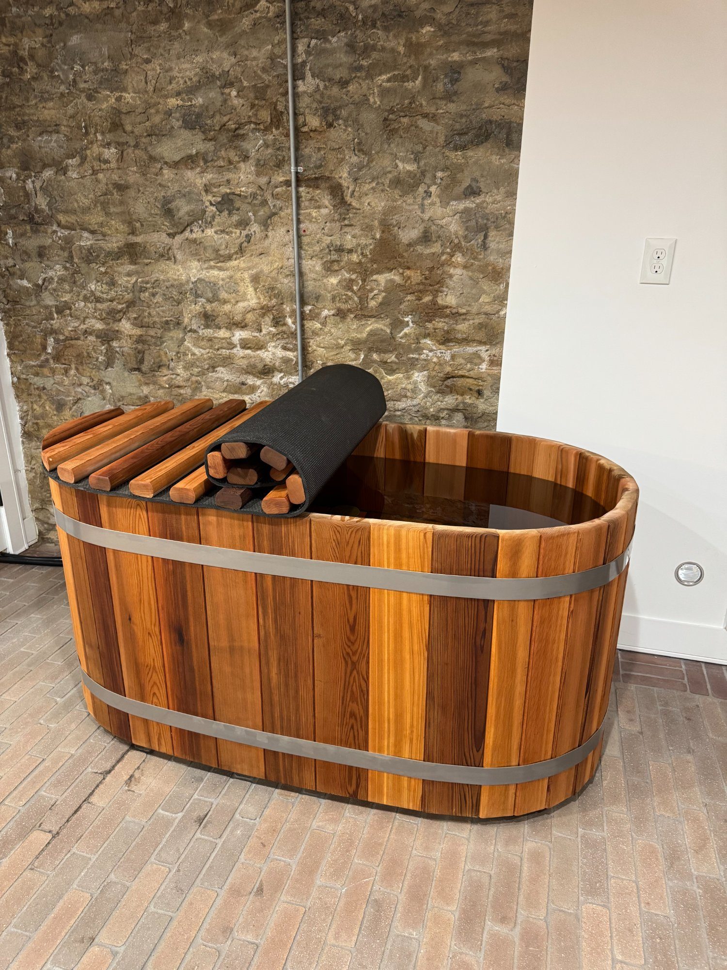 Handcrafted cedar cold plunge tub with stone wall background St. Louis
