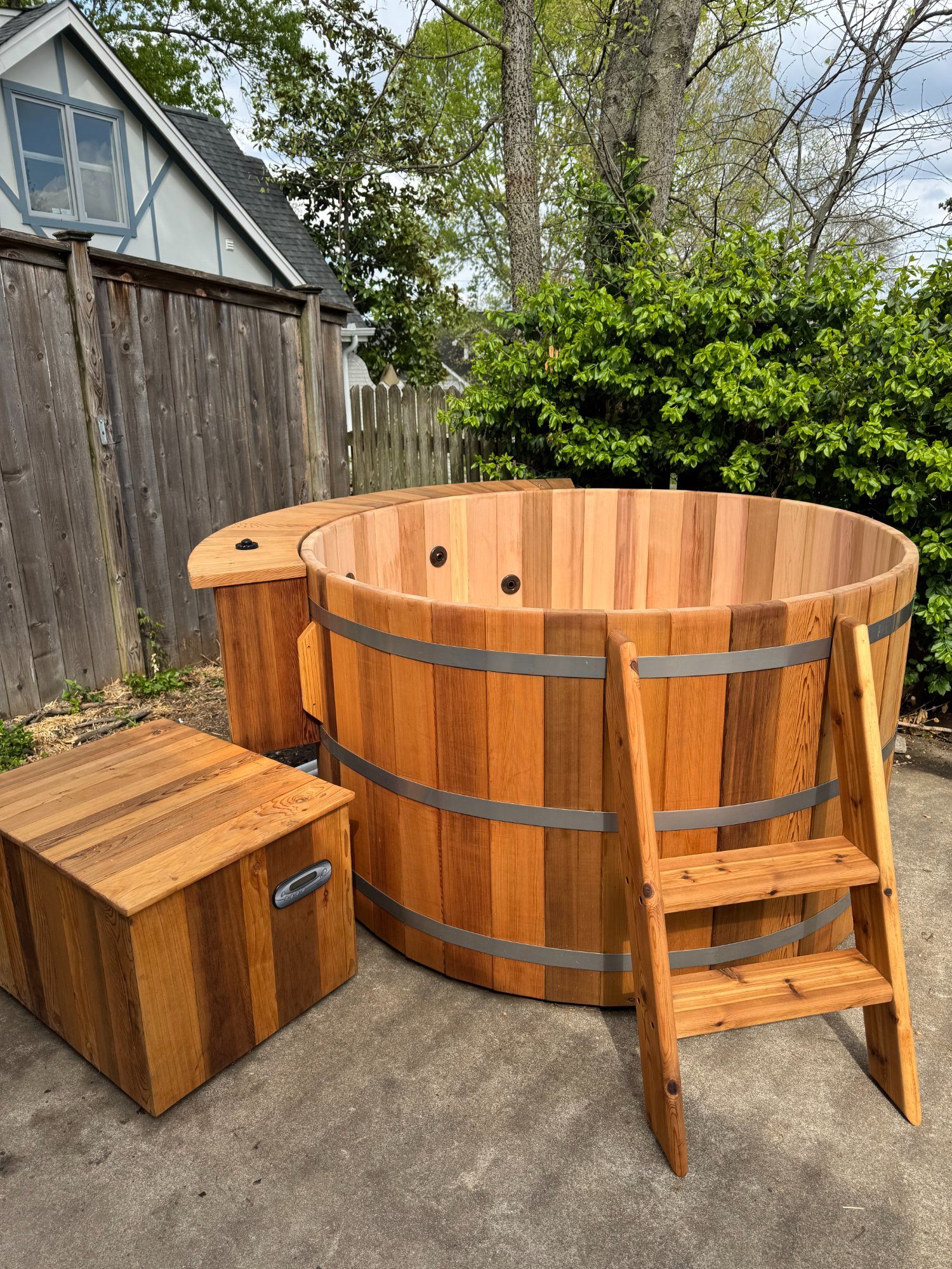 Clean cedar hot tub with ladder and equipment box in a backyard setting