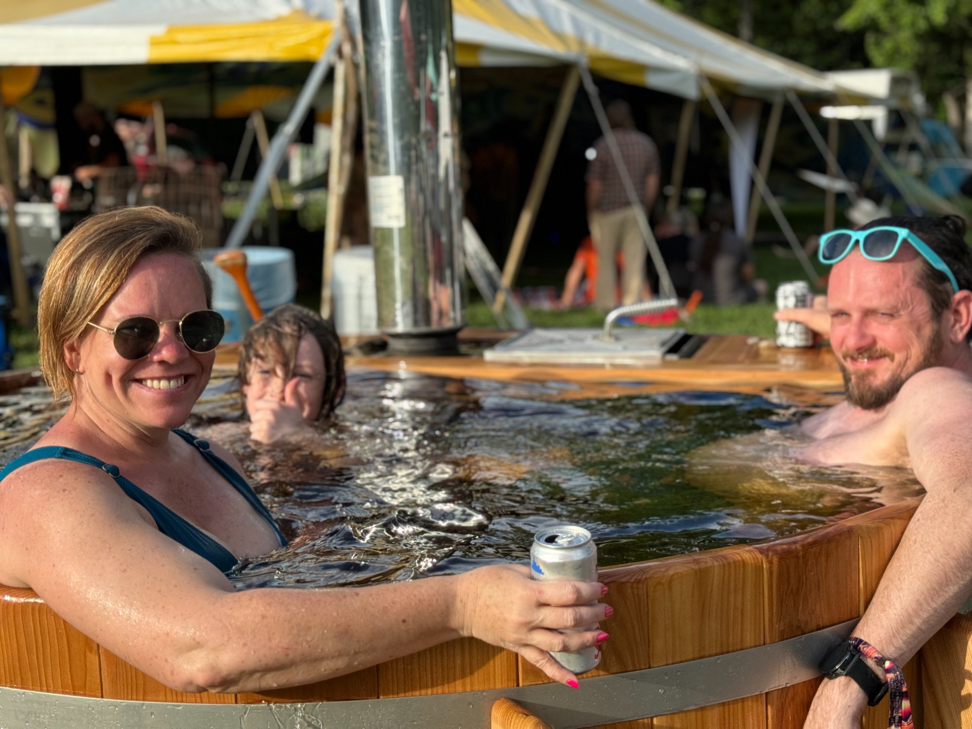 Family enjoying a cedar hot tub at a summer outdoor event, smiling in the warm water