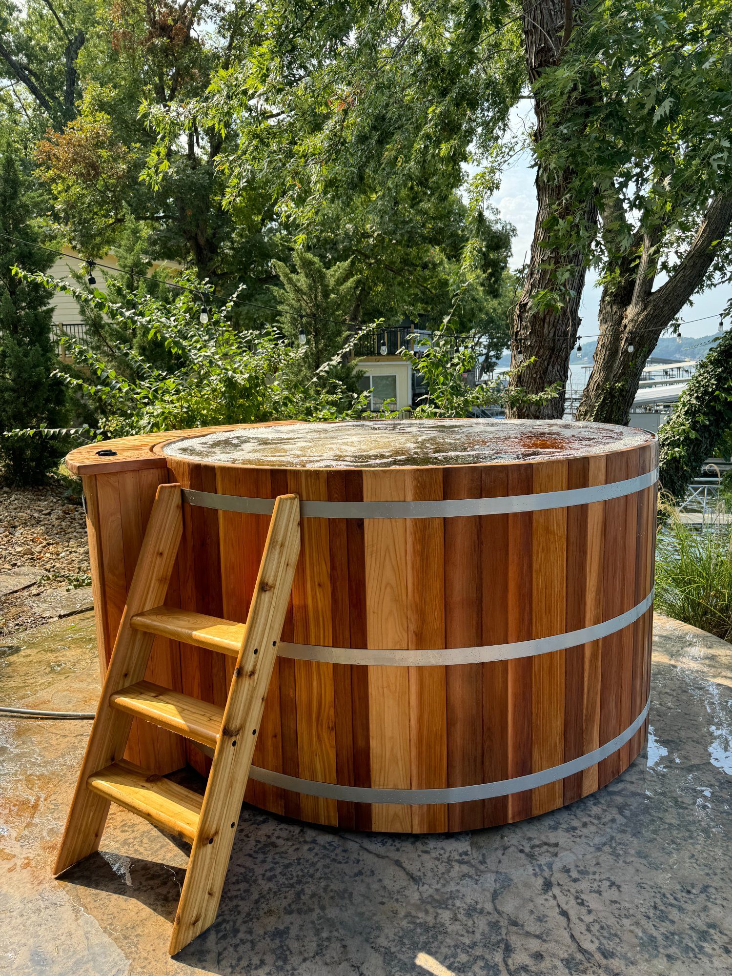Large cedar hot tub with ladder installed lakeside with bubbling water
