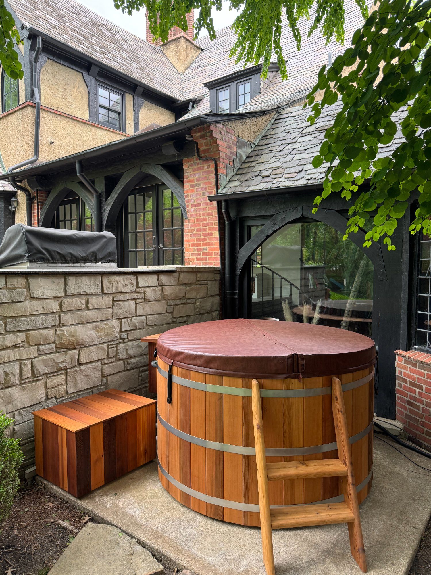 cedar hot tub with cover installed against stunning Tudor-style home with stone walls