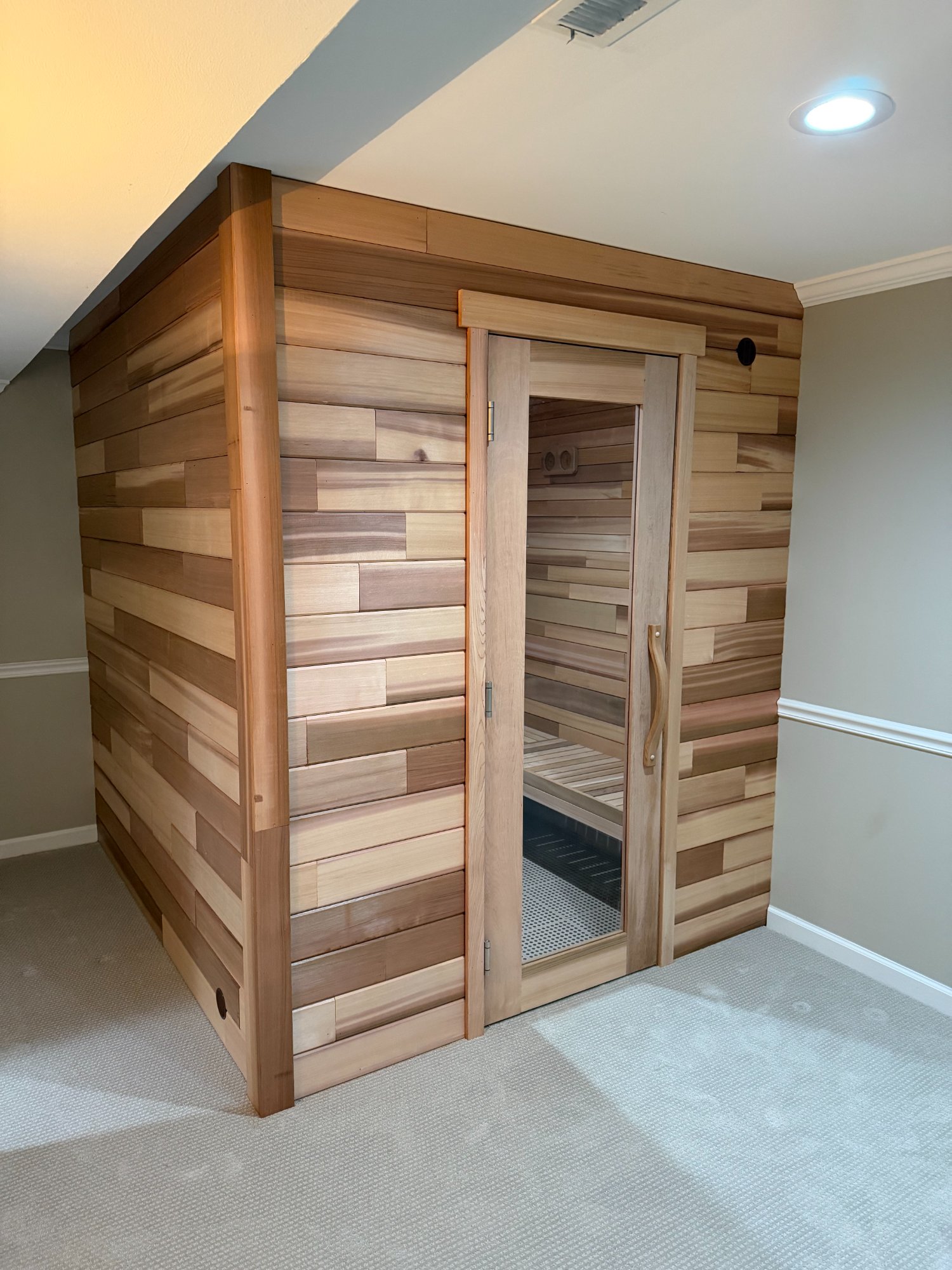 Custom cedar sauna with staggered cedar exterior paneling built into a finished basement room
