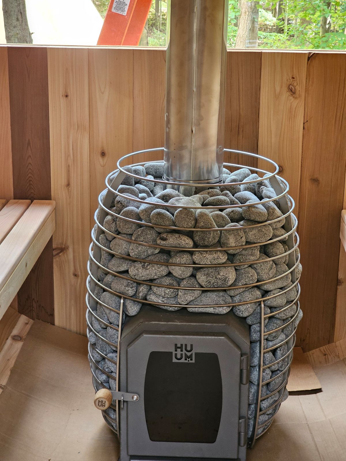 HUUM wood-burning sauna heater with river stones in outdoor cedar sauna