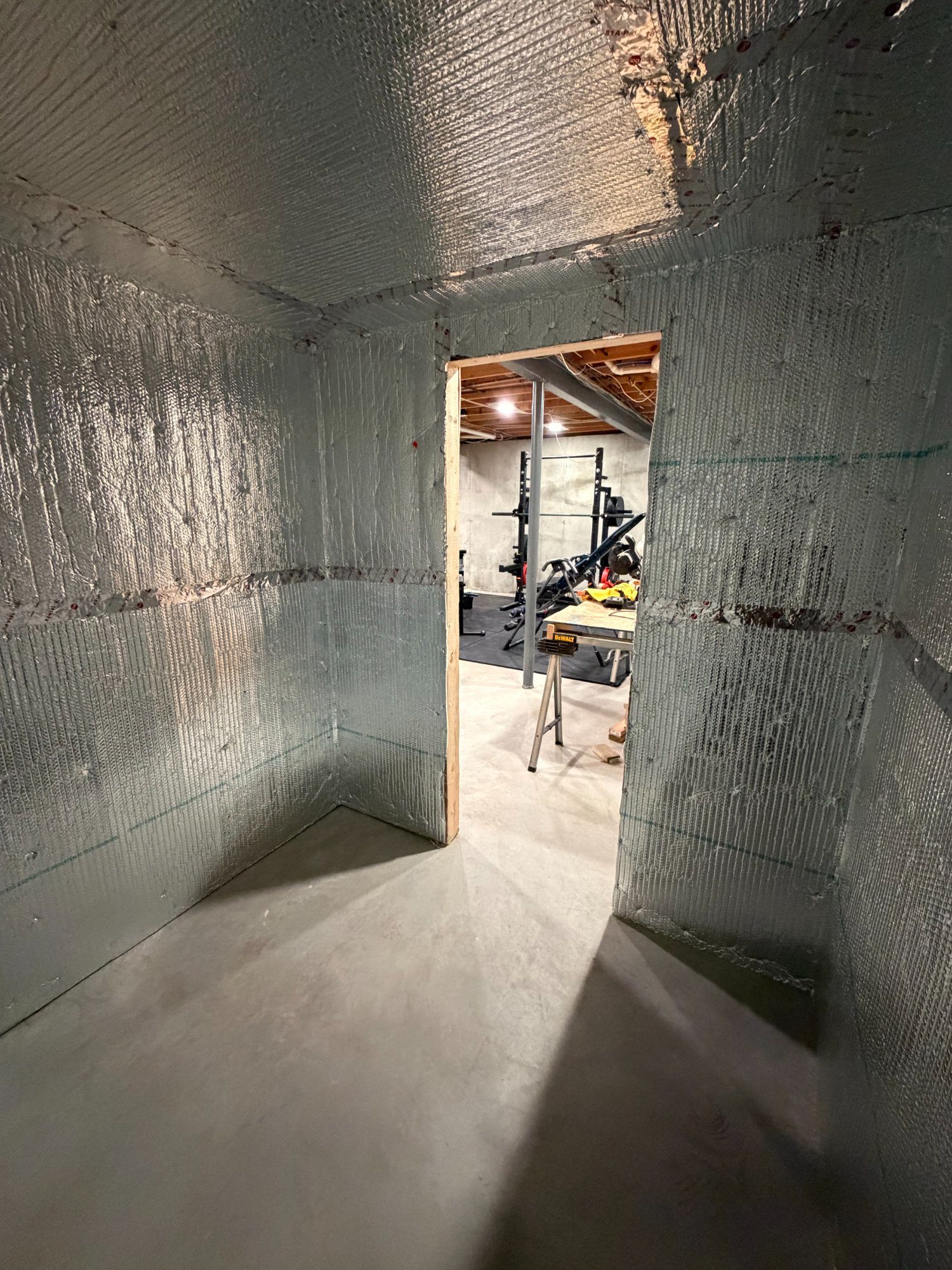 Foil insulation barrier fully applied inside sauna room looking through doorway to home gym