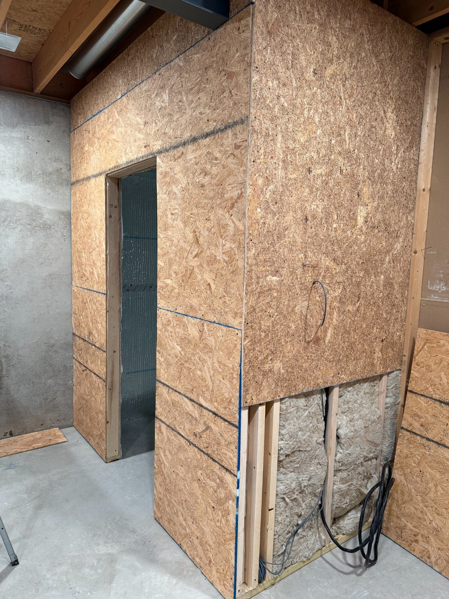 OSB sheathing on exterior of sauna structure with foil insulation visible through door opening
