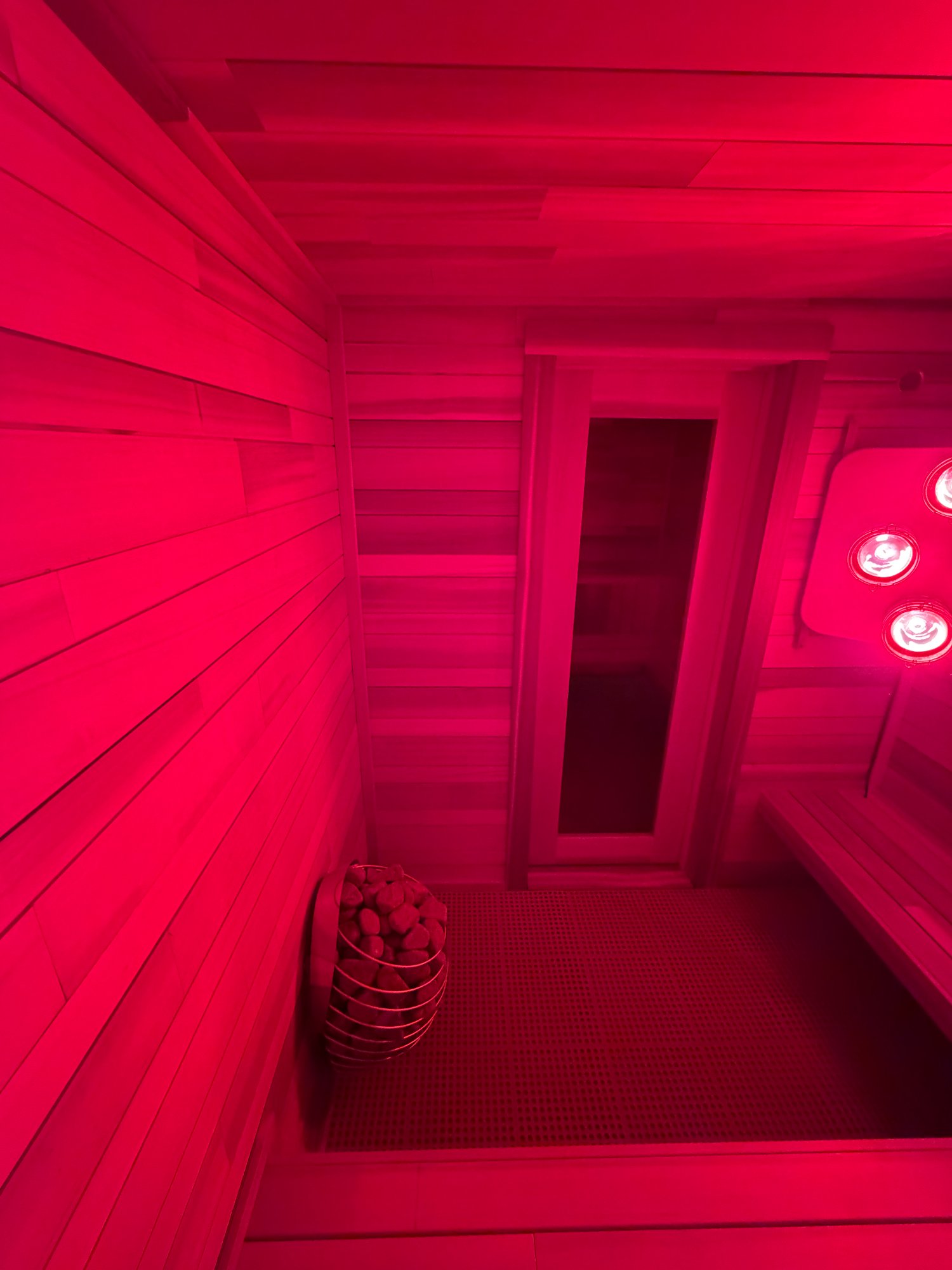 cedar sauna interior bathed in red infrared light therapy with HUUM heater visible
